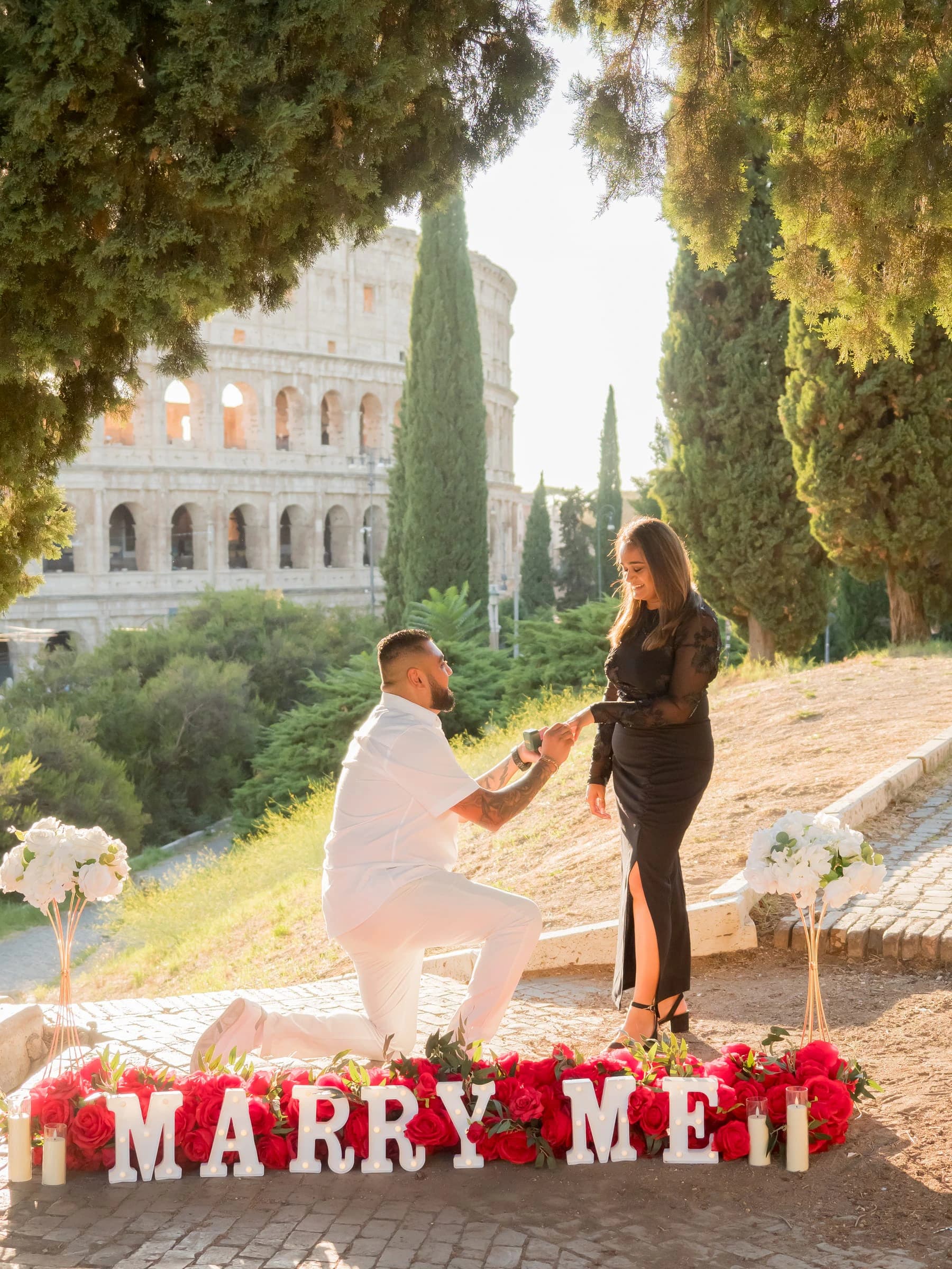 He kneels behind Marry Me letters and roses, the Colosseum at golden hour