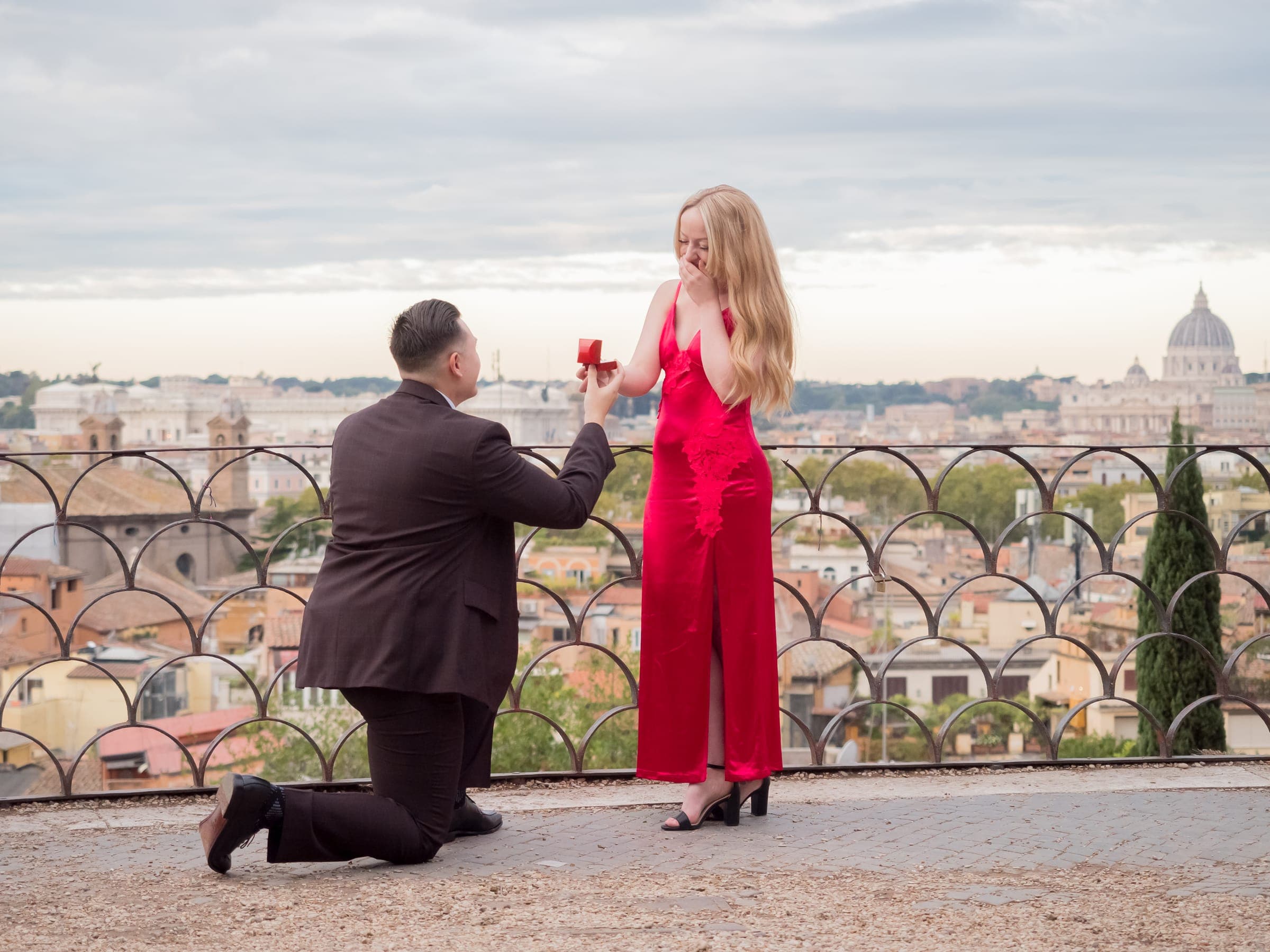 He kneels at the Pincian terrace railing, she in red laughs, St Peter’s dome on the skyline