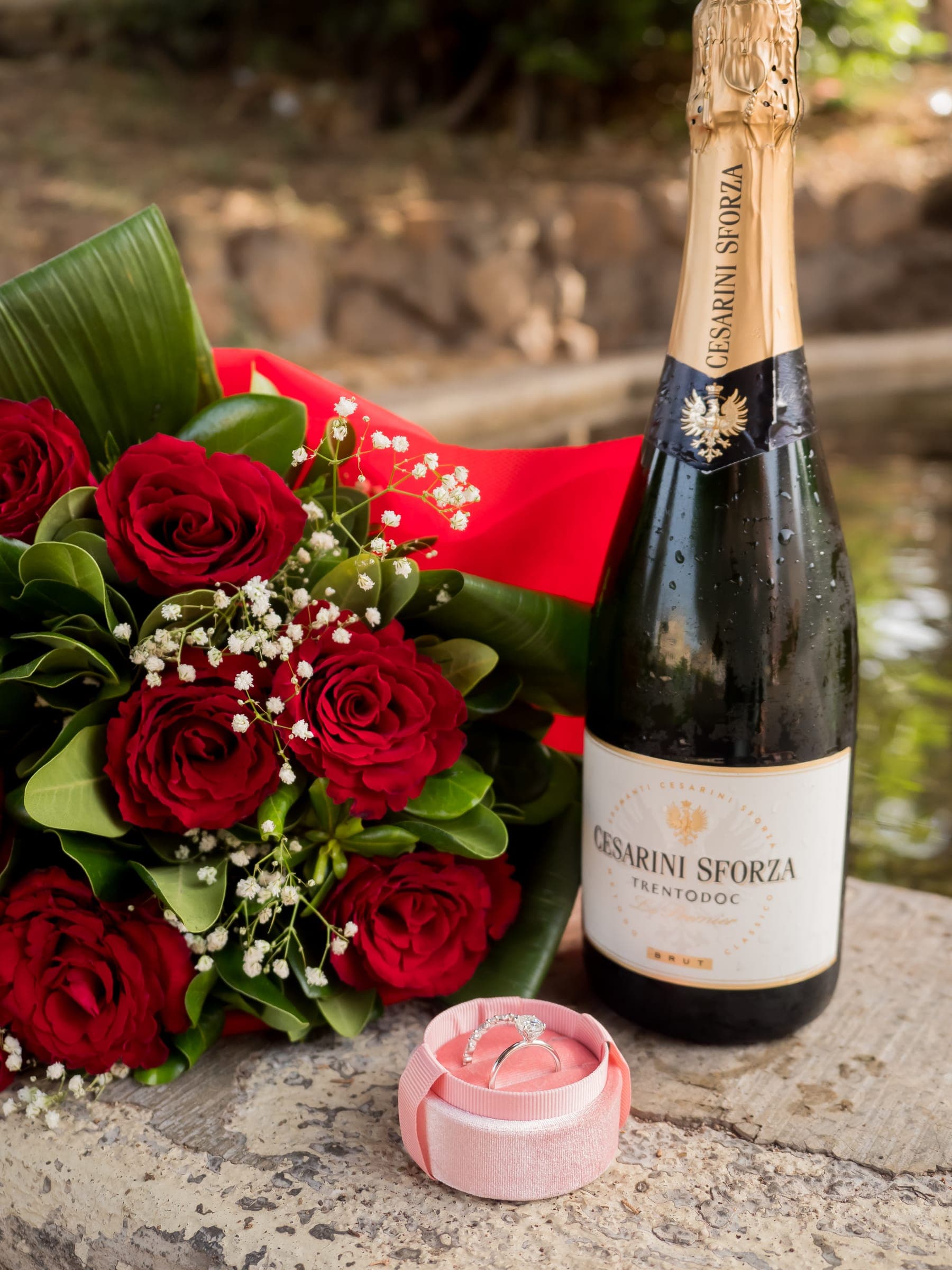 Red roses, a ring box and a bottle of prosecco on a stone ledge